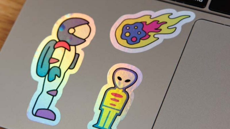Colorful stickers of an astronaut, an alien, and a comet on a laptop surface.