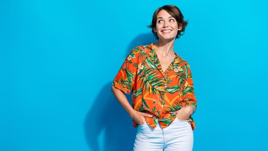 A woman wearing a colorful orange AOP shirt with a pattern of leaves and flowers.