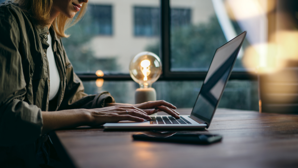 A woman in a green shirt typing on a laptop with a blurred bulb in the background.