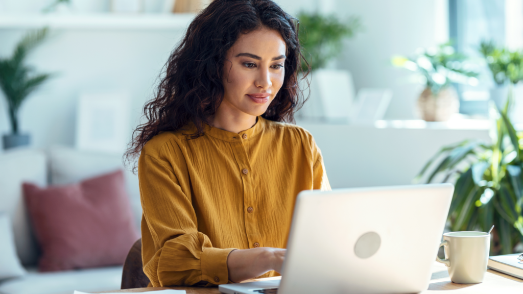 A woman sitting at a desk in front of a laptop and looking at the screen.
