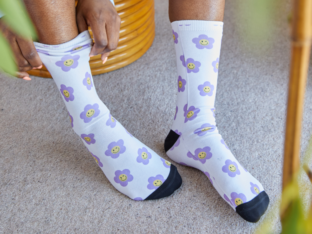 A person wearing purple and white floral socks showcasing a vibrant and playful design on their feet.