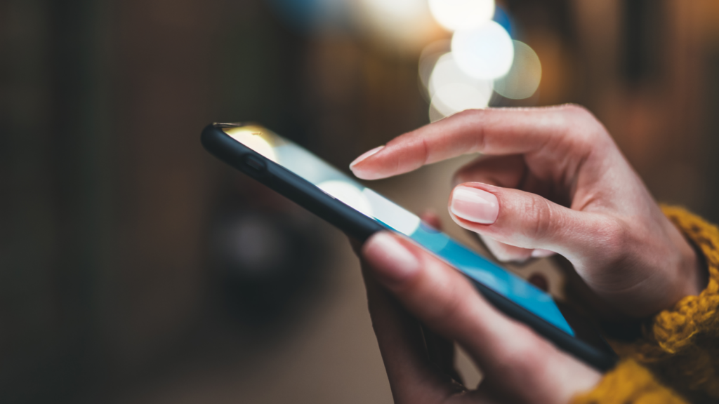 A person holding a mobile phone in one hand and tapping the screen with the other hand.