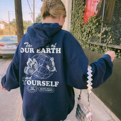 A woman wearing a blue hoodie that has a social message on it about taking care of earth and yourself.