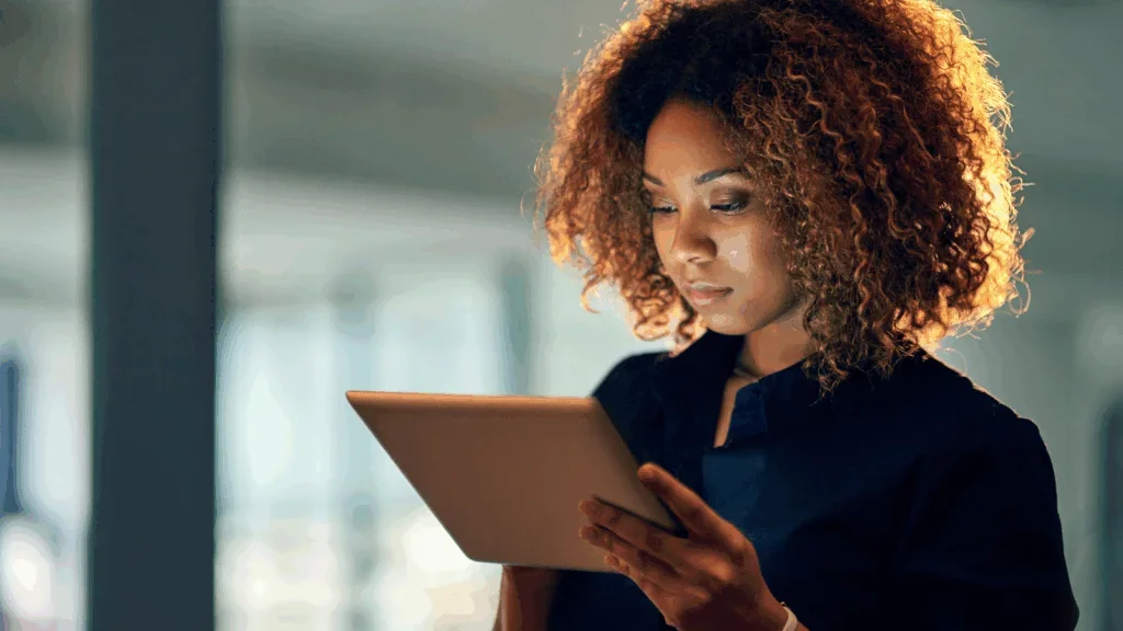 A woman in a blue blouse standing and looking at a tablet screen.