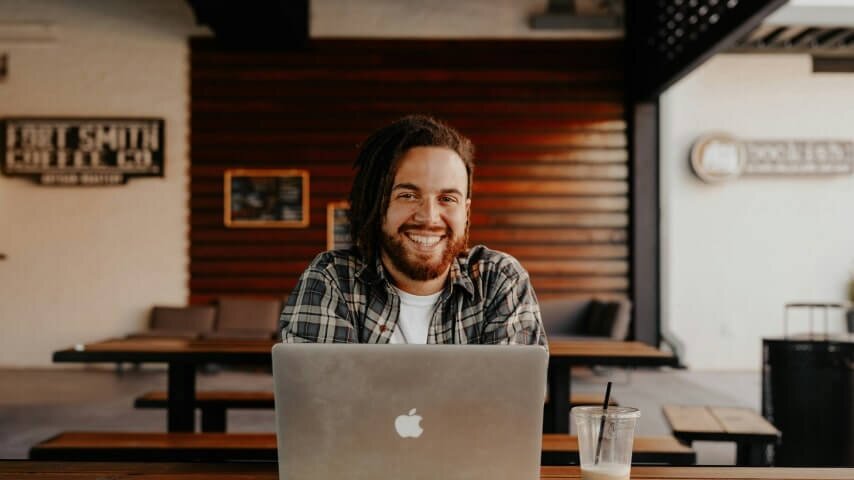 A smiling man sitting in front of a laptop.