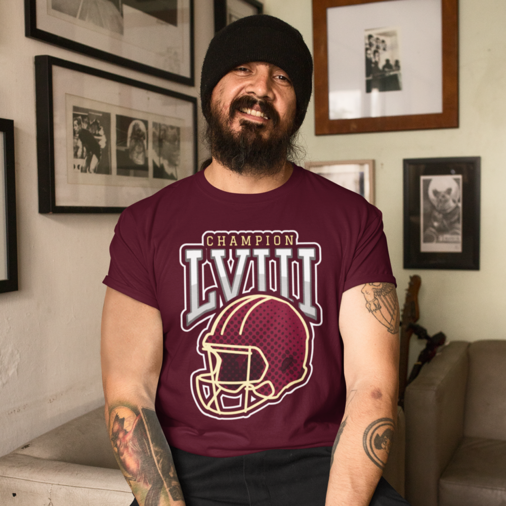 A man with a beard and tattoos, wearing a maroon "Champion LVIII" football helmet shirt, smiles indoors.