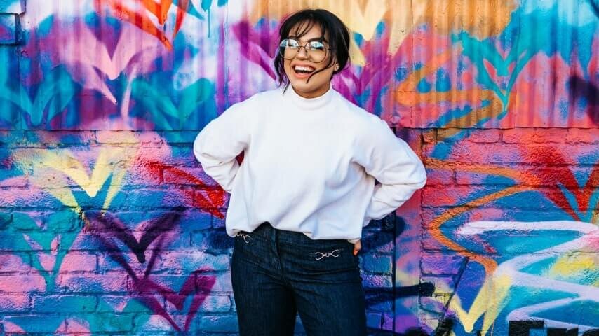A woman laughing in front of a colorful background wall.