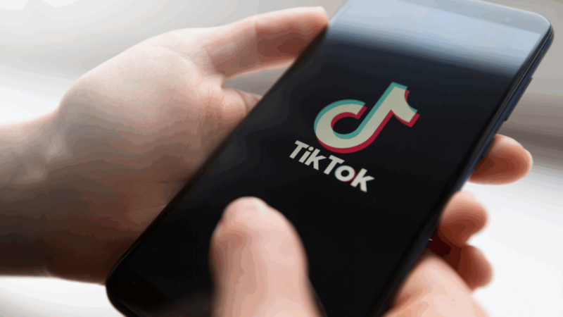 A person is holding a mobile phone with the TikTok app loading screen.