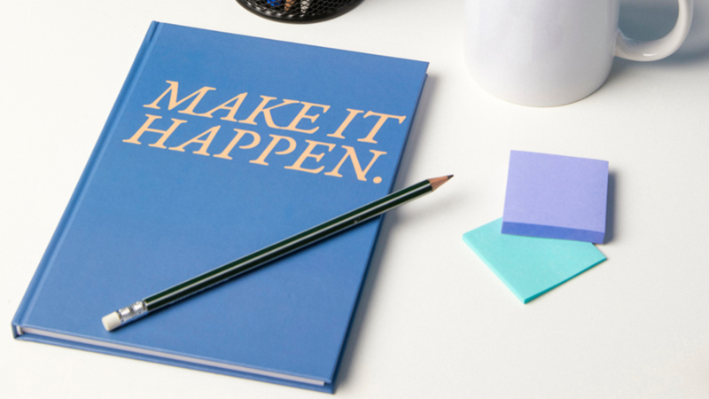 Notebooks: A custom notebook titled "Make It Happen" rests beside a pencil and a coffee cup on a wooden table, inviting inspiration.