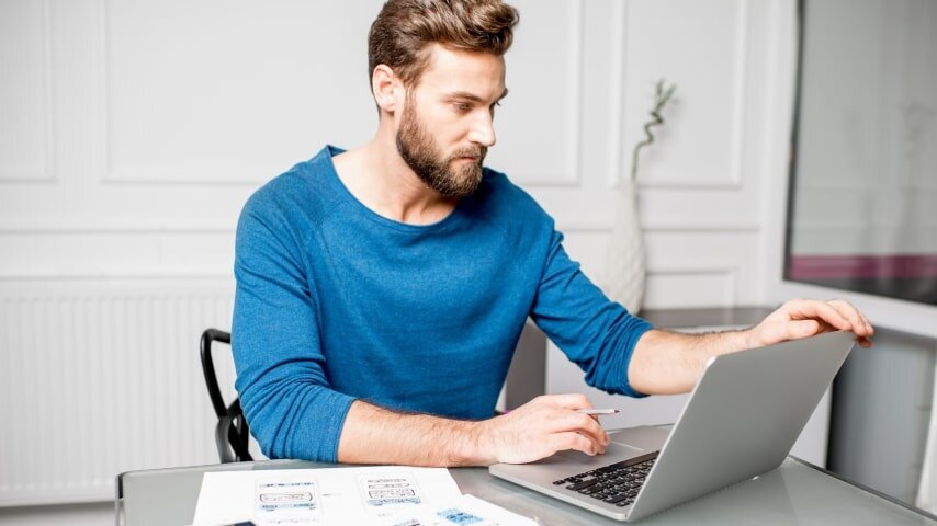 A man working on his laptop to create designs for digital planners to sell on Etsy.