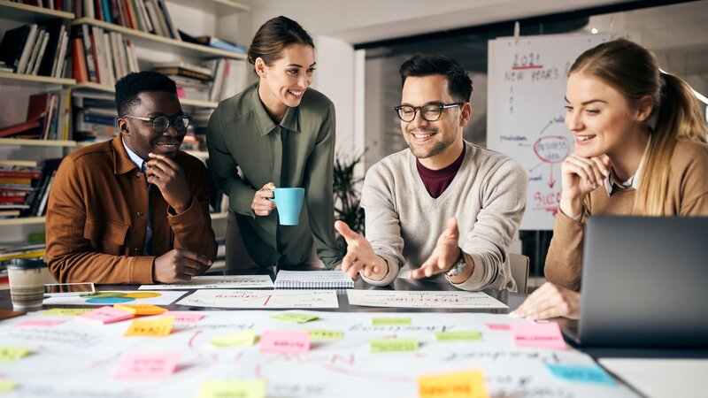 A diverse group of individuals collaborates around a table covered with colorful sticky notes.