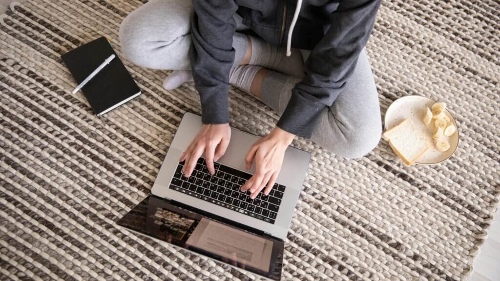 A person sitting on a rug and using a laptop for work.