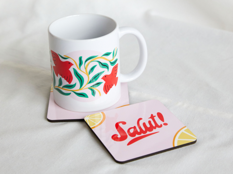 A coffee mug and coaster featuring the word "salut" elegantly displayed on a wooden surface.