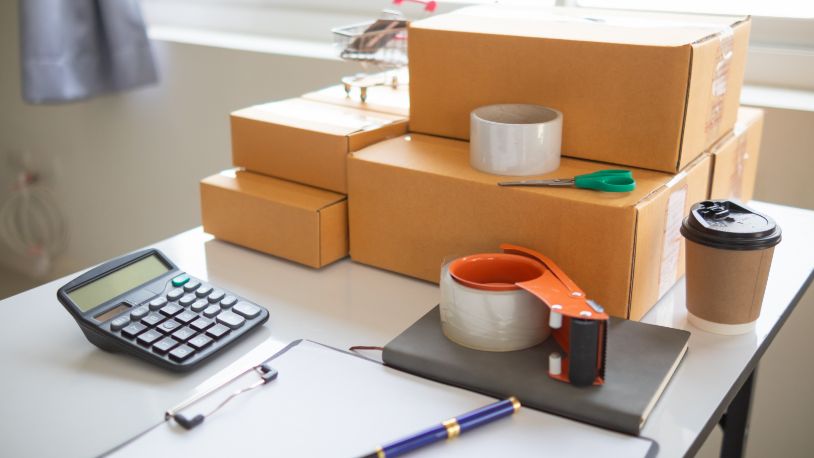 A stack of delivery boxes on top of a table with miscellaneous office supplies around it.