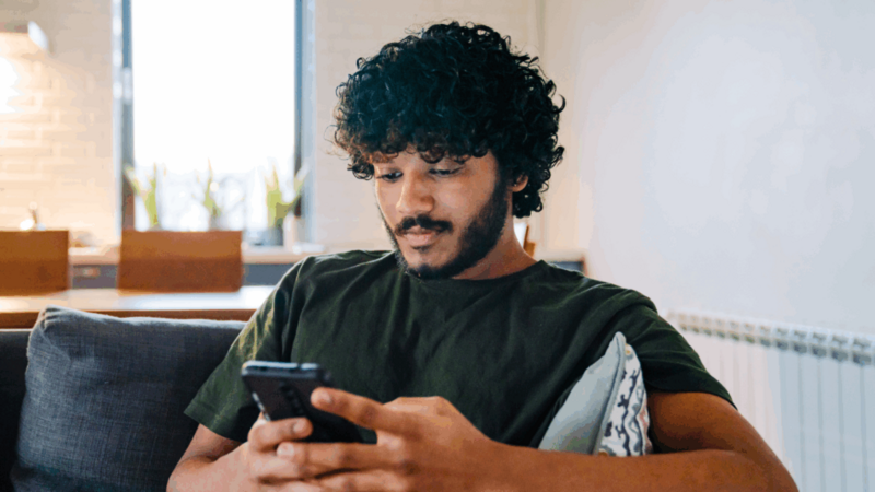 A young man is sitting on a couch and using a mobile phone to learn how to start dropshipping for free.