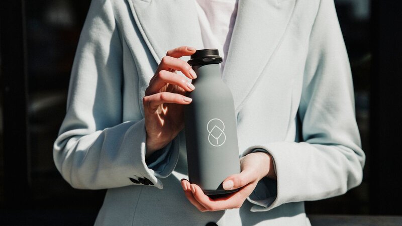 A person holding a gray insulated water bottle with a logo on it, wearing a light blue blazer.
