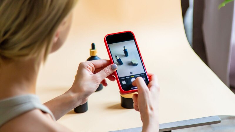 A person is taking a photo of beauty products with a smartphone on a wooden table.