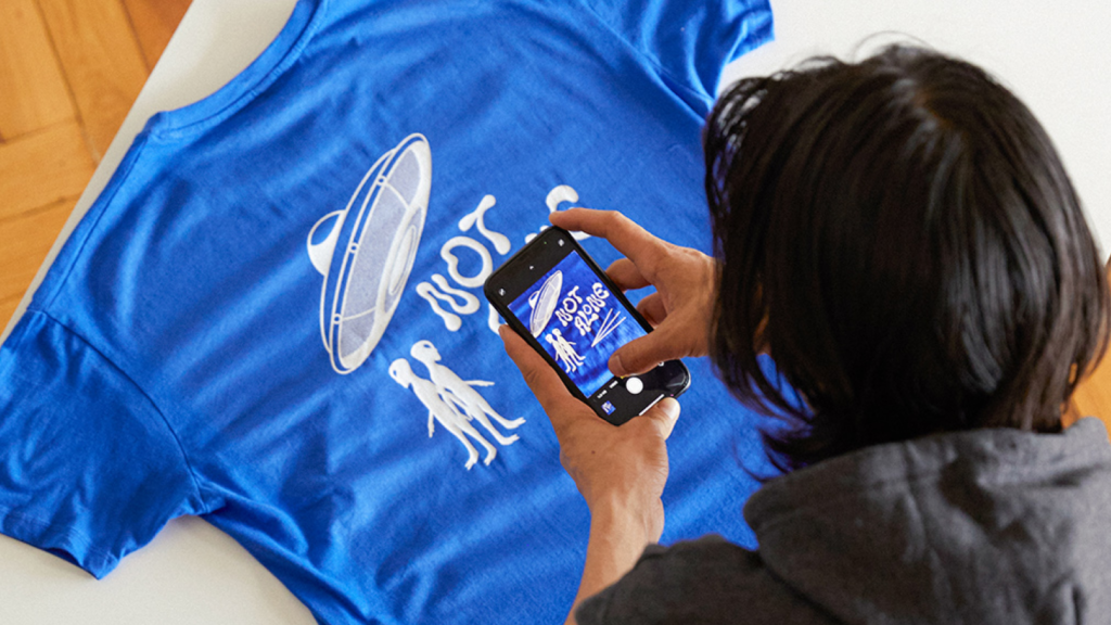A person taking a picture of a custom blue t-shirt.