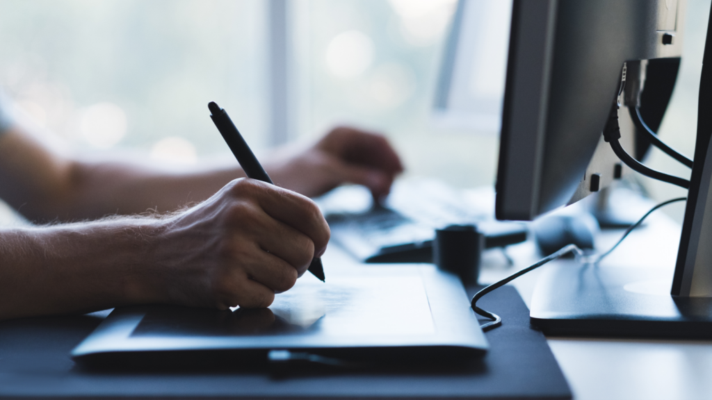 An individual engaged in computer work, using a pen to jot down ideas, illustrating a blend of technology and traditional methods.