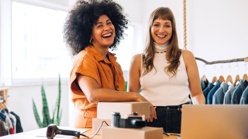 Two women standing in front of a desk with delivery boxes and smiling.