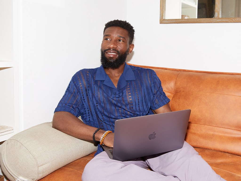 A man comfortably sitting on a couch, working on his laptop to create an online store.