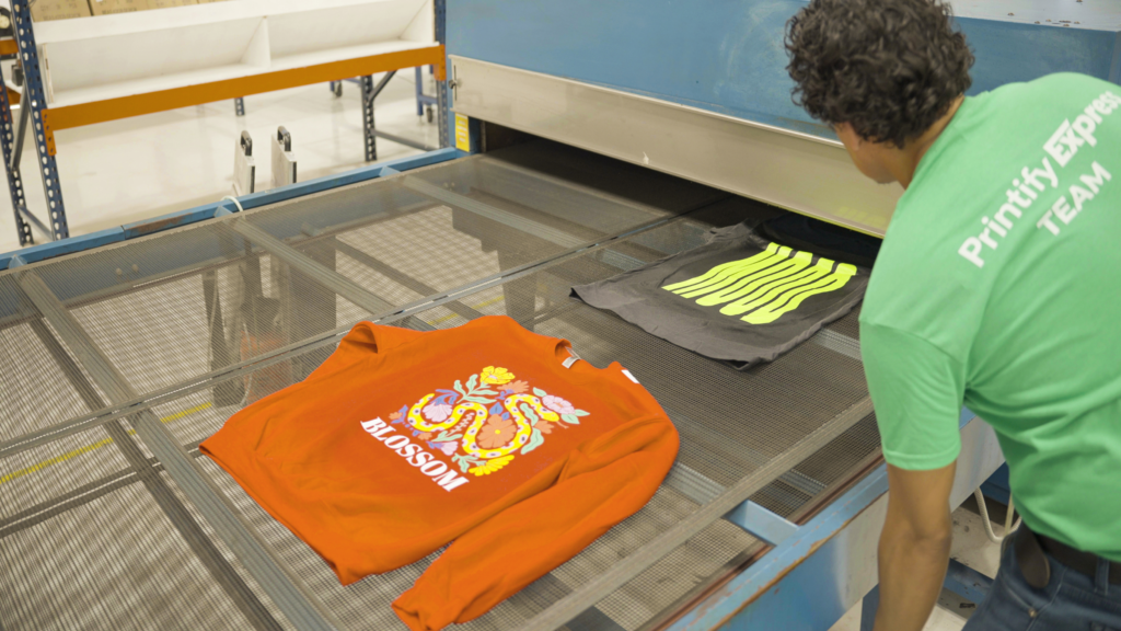 A man from the Printify Expert team is working on an orange sweatshirt.