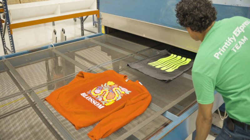A man from the Printify Expert team is working on an orange sweatshirt.