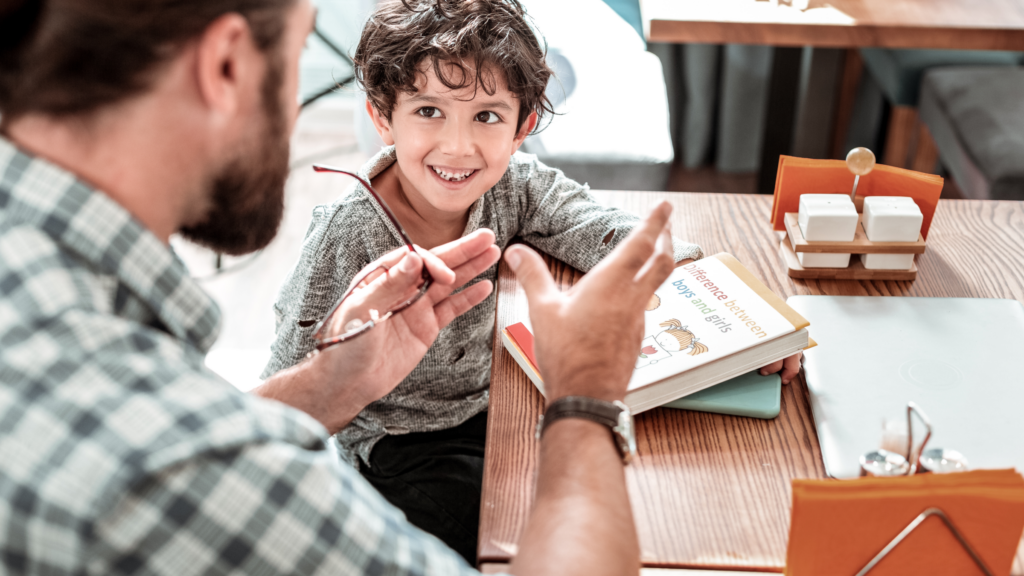 A man and a boy are seated at a table, surrounded by books, engaged in a thoughtful discussion.
