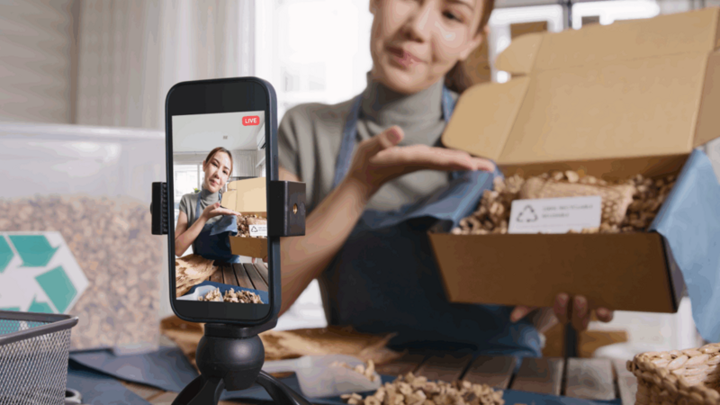 A woman live-streaming using a mobile phone, showcasing products.