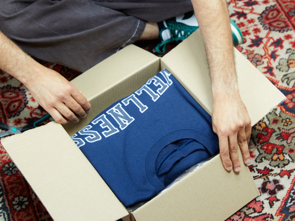 A person unpacking a delivery box with a blue hoodie inside.