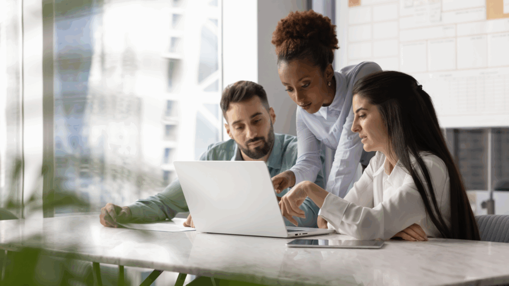 Three individuals gathered around a laptop, intently discussing its screen content.