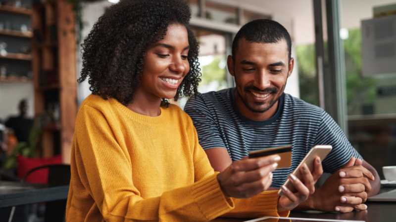 A couple at a coffee shop, smiling as they use a credit card to pay for their drinks.