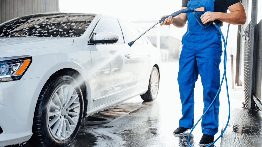 A man in overalls washes a white car.