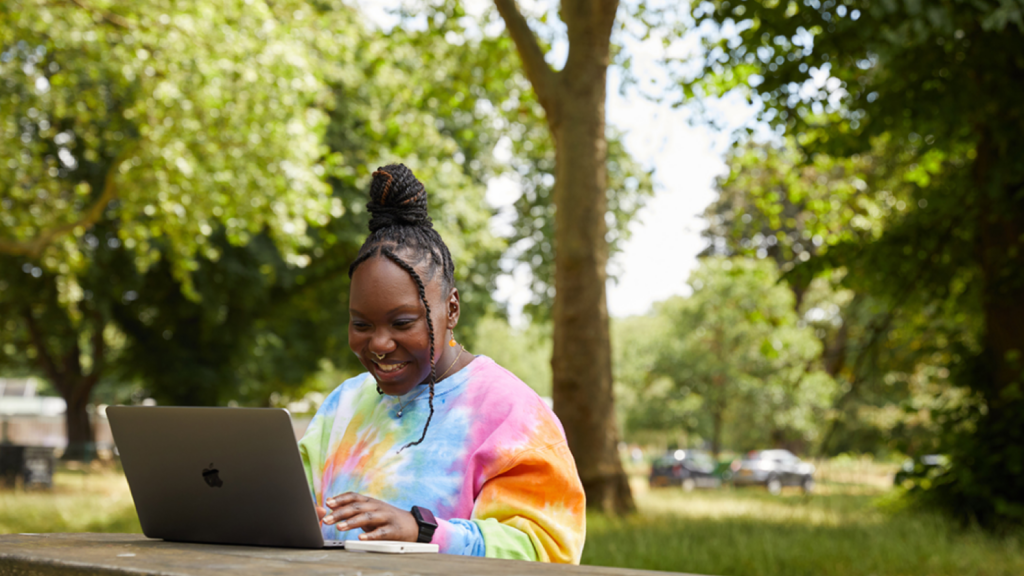 A young woman working from her laptop in a park.