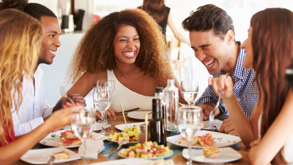 A group of friends enjoying dinner together at a restaurant, smiling and sharing food around a table.