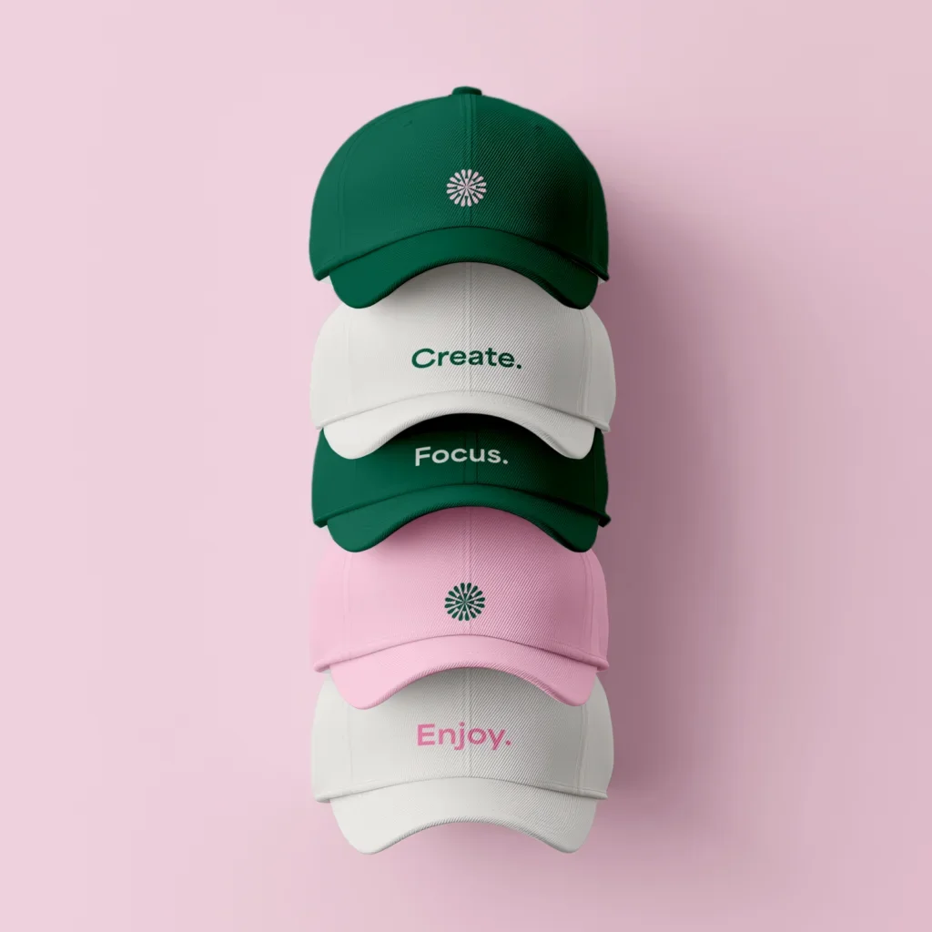 White, green, and pink hats with text or logo prints stacked on top of each other on a pink background.