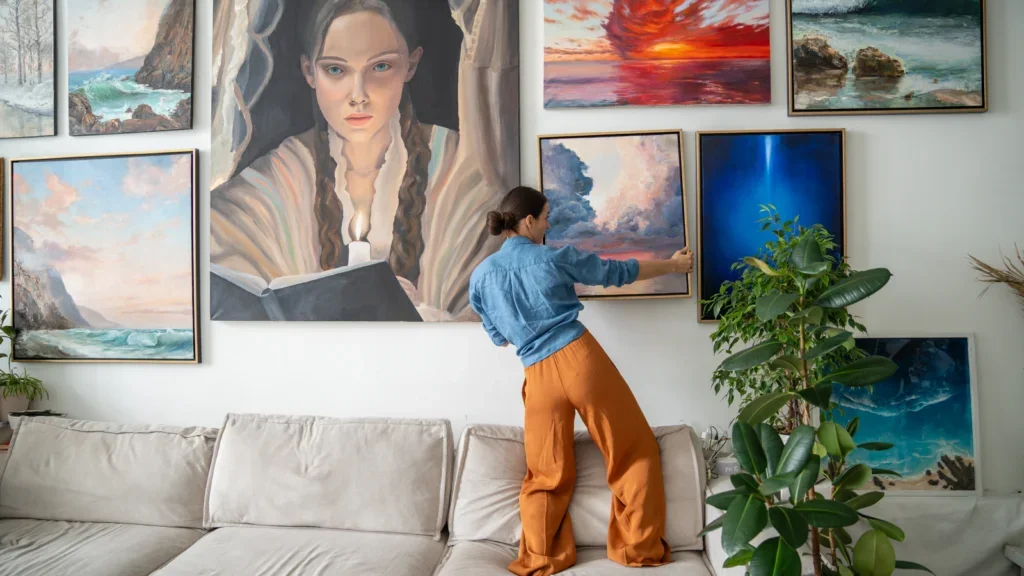 A woman hanging a painting on a wall full of paintings.