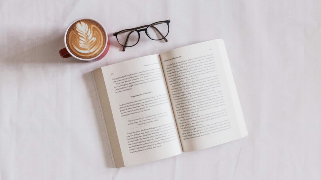 A book, a cup of coffee, and glasses arranged on a table, creating a cozy reading atmosphere.