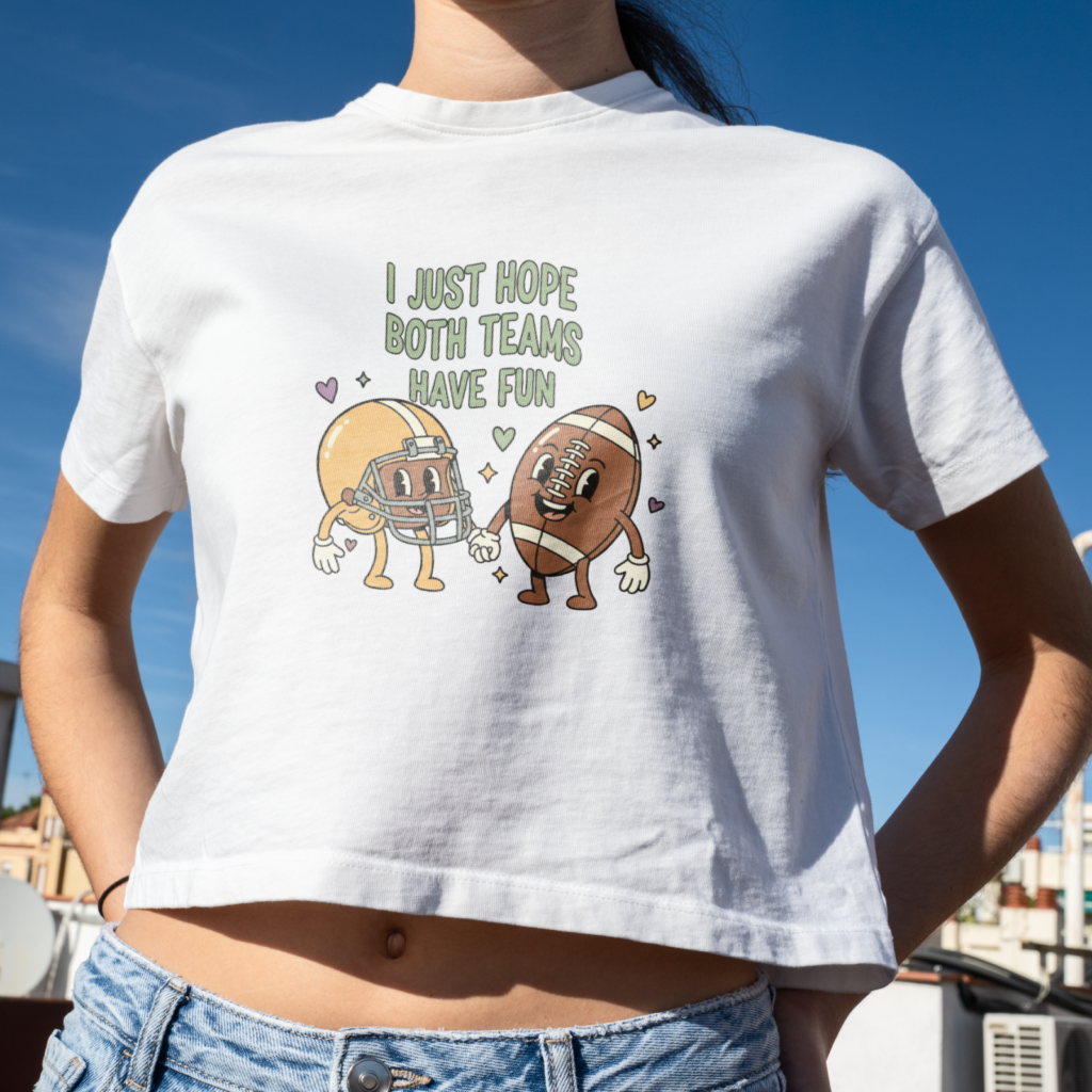 A woman wearing a white crop top with cartoon football and helmet characters holding hands, reads "I just hope both teams have fun".