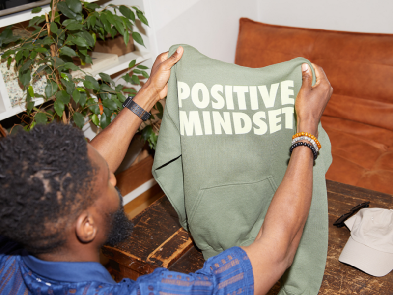 A man is holding a green “Positive Mindset” hoodie.