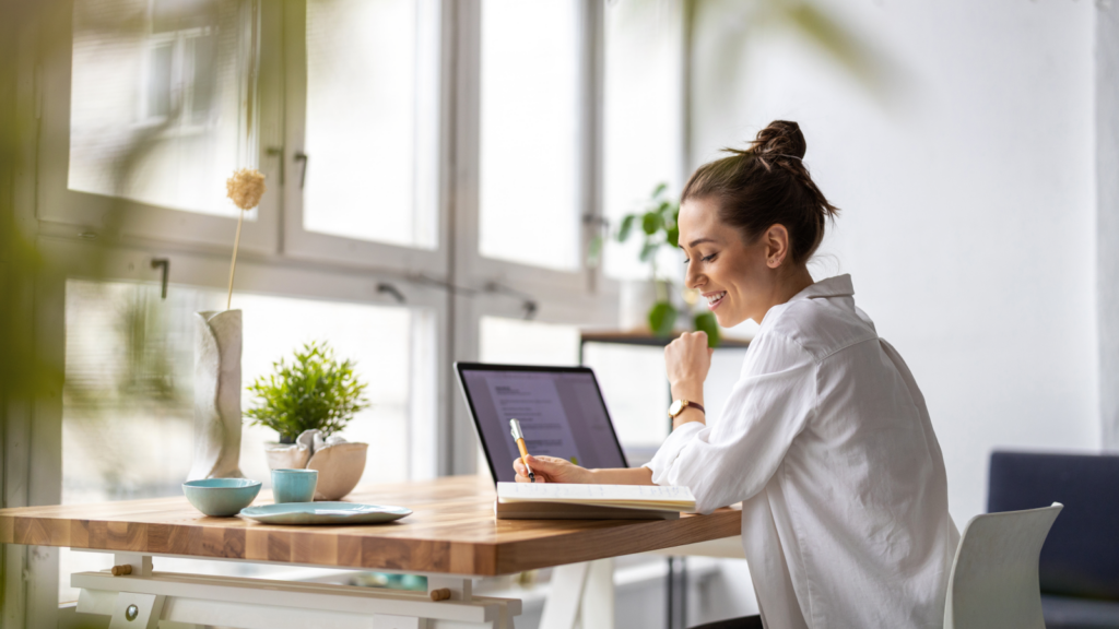 A woman seated at a table, focused on her laptop, engaged in work or study.