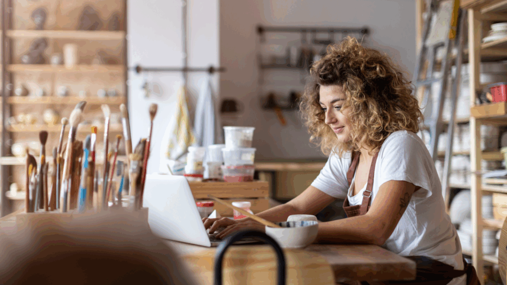 An artist is sitting in a studio, using a laptop.