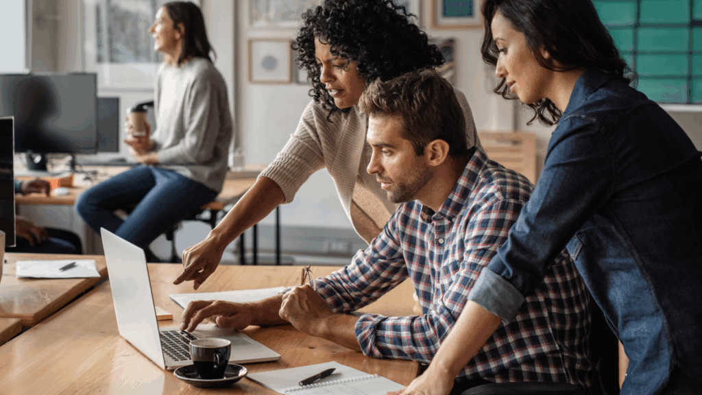 A group of diverse individuals collaborating on a laptop in a modern office setting.