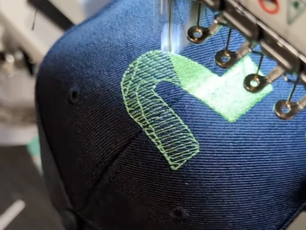 A person is sewing a hat featuring a green arrow design on the front