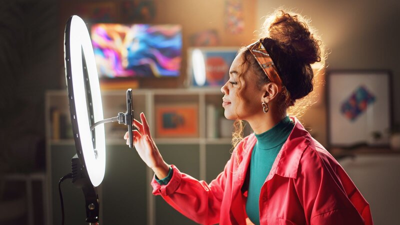 A woman holding a canned beverage and recording herself on a mobile phone.