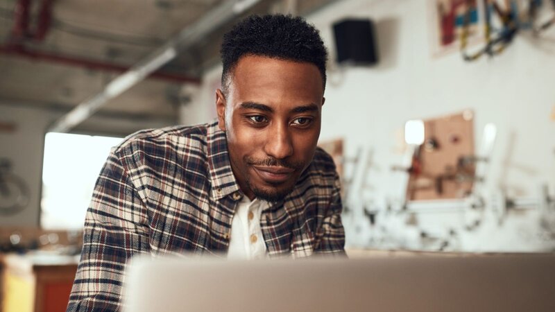 A man in a flannel shirt is curiously looking at a laptop display.