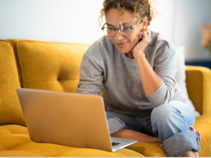 A woman sits on a couch, focused on her laptop, exploring best-selling items on Etsy.