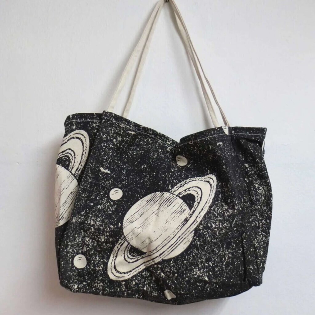 A large tote bag with Saturn surrounded by stars and other planets.