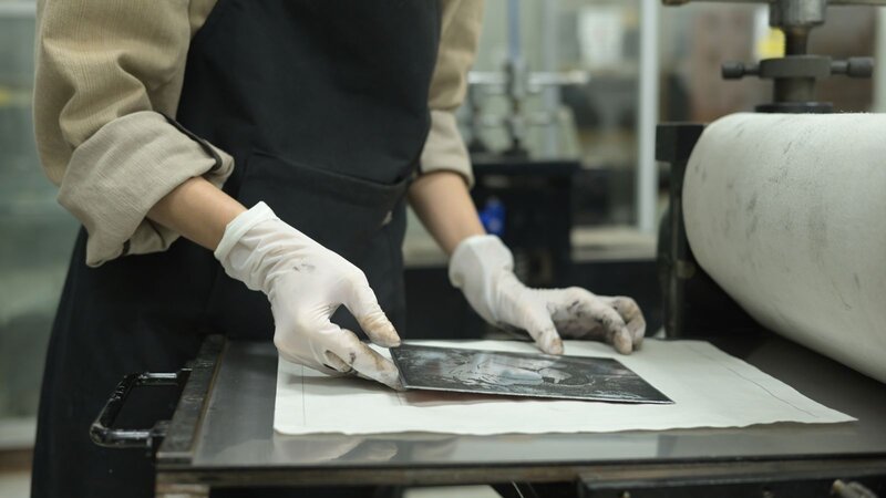 A person is preparing a piece of metal for etching.