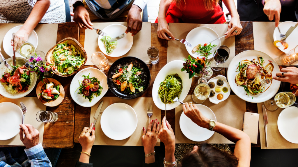 Several individuals seated at a table, sharing a meal with an assortment of dishes and plates of food displayed.